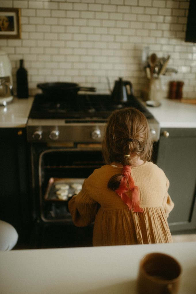 little girl putting cookies in the oven