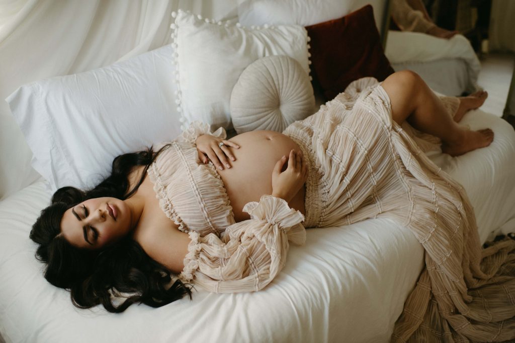 pregnant woman lying on bed in flowy dress