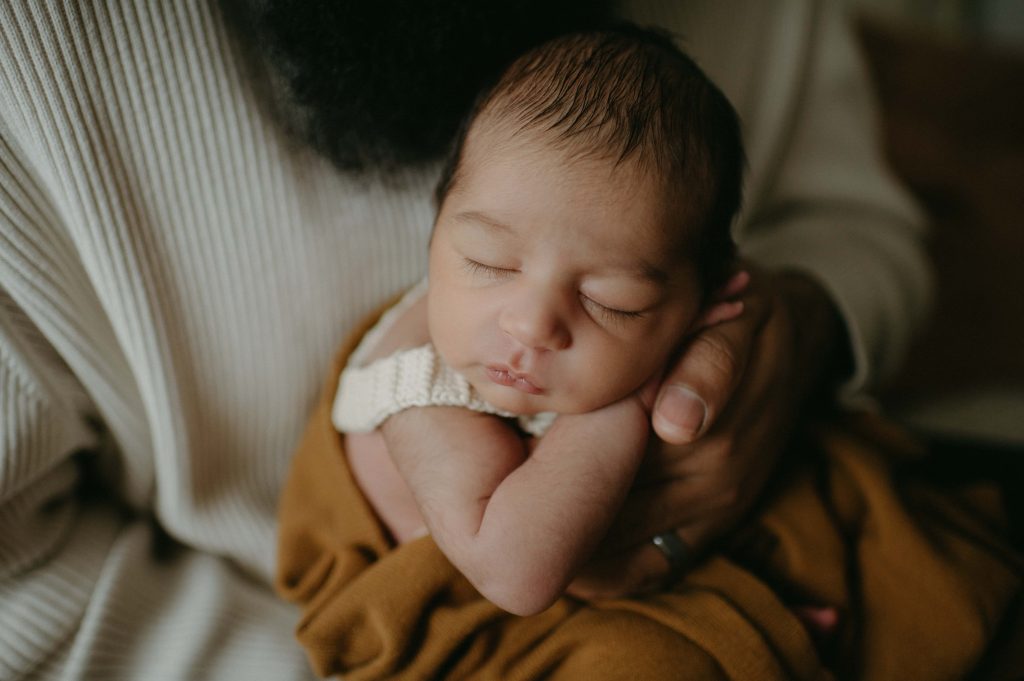 Newborn in dad's hands resting head on arm