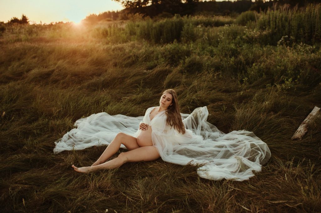 pregnant woman at sunset sitting in long grass at beach