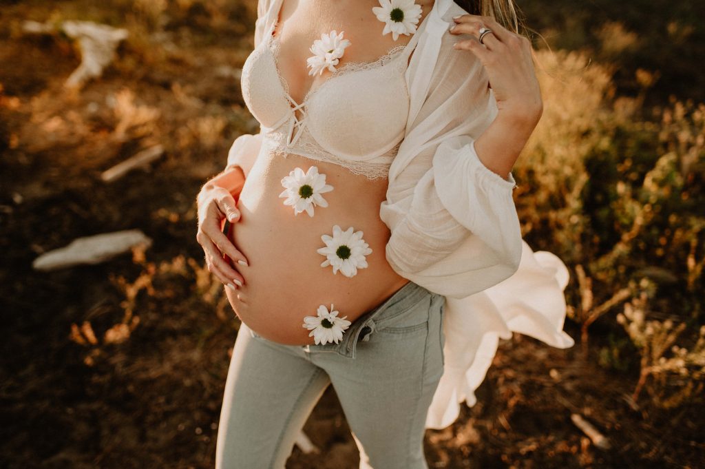 pregnant belly with flowers on white rock beach