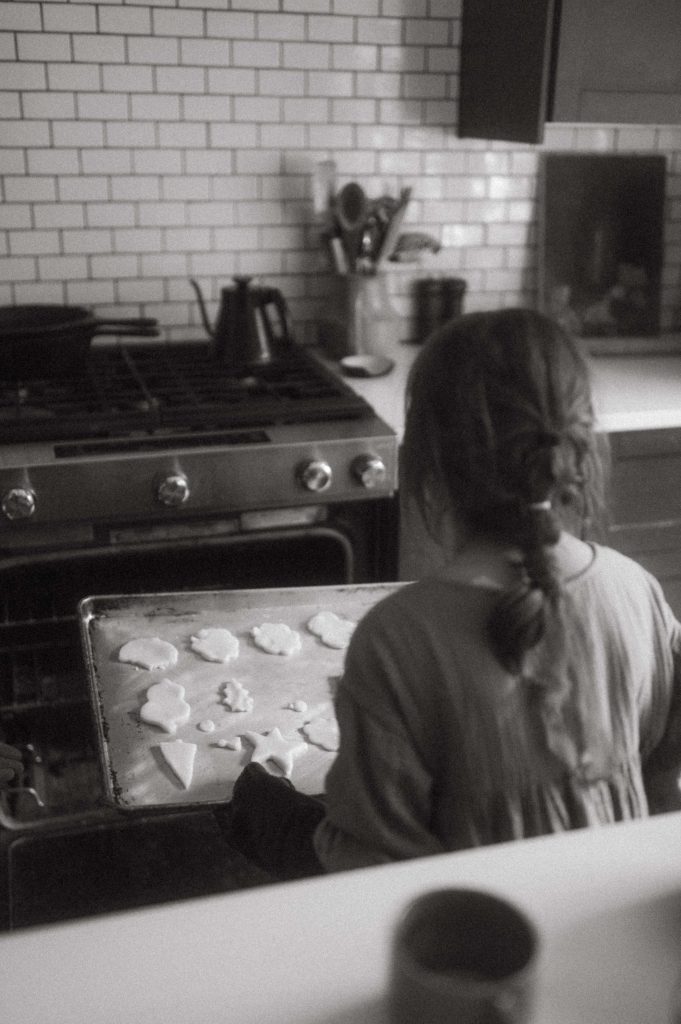 little girl putting cookies in oven black and white