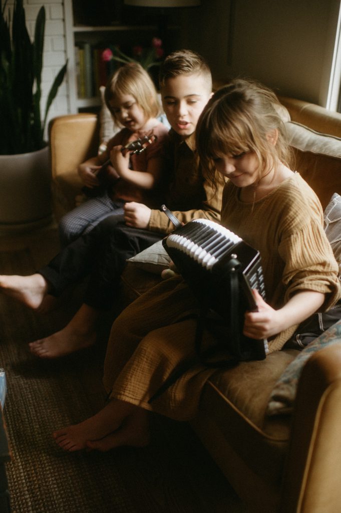 little girl playing accordion with siblings beside her